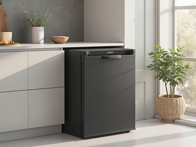 A black under-counter refrigerator with a sleek design and a handle is positioned next to a light-colored cabinet. The control panel is located on the top of the door, and the refrigerator has a modern appearance, suitable for residential settings.
