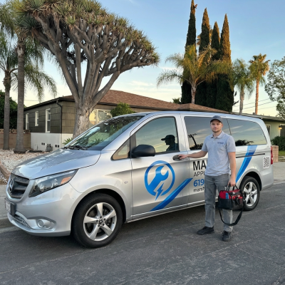 Silver appliance repair van with blue wrench graphic and blue stripe; technician in gray polo stands beside the van, holding a red tool bag.